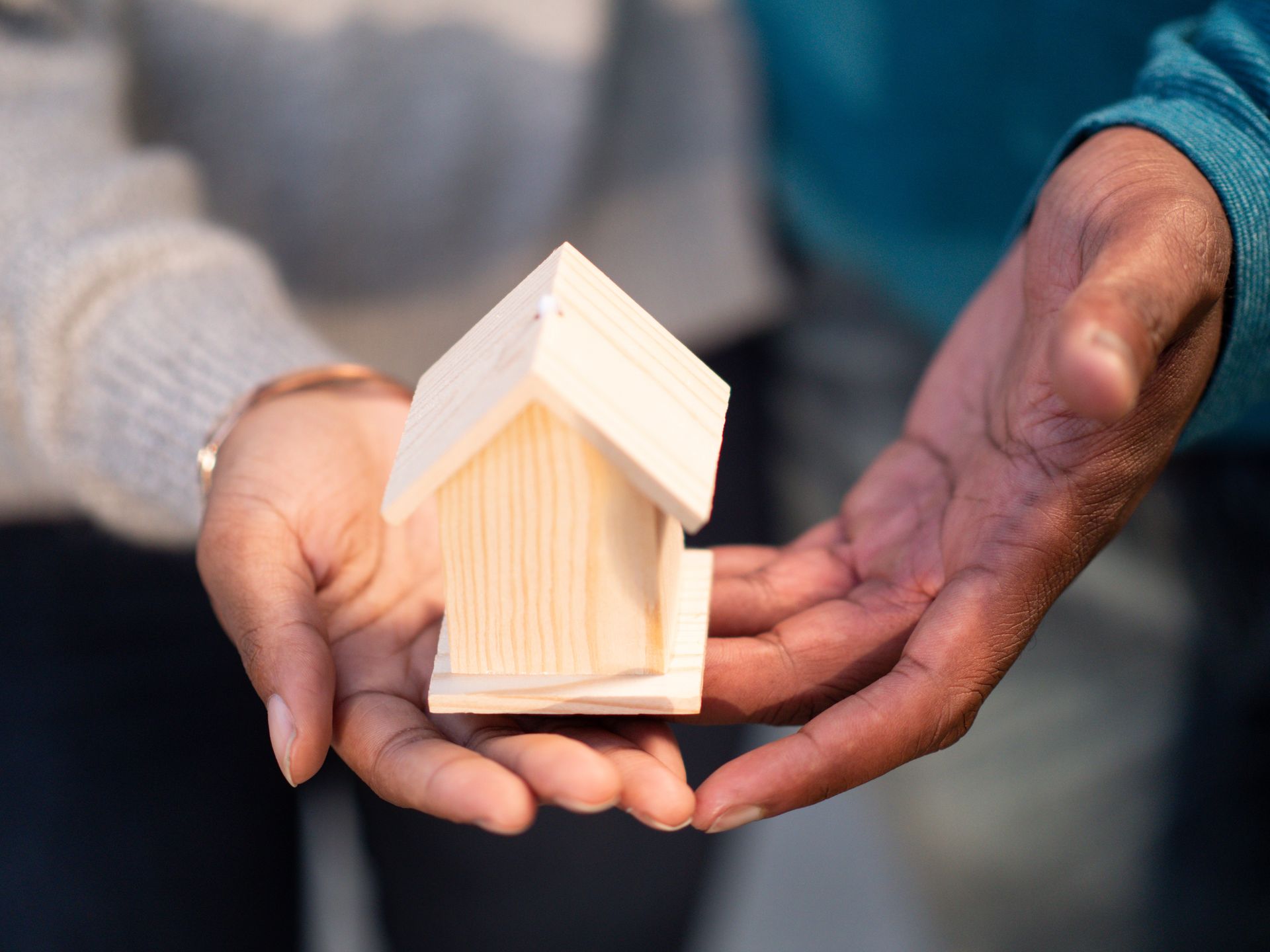 Two hands come together to hold a small, wooden house made out of light-coloured wood to illustrate affordable housing for an article by Angela Grogan, Port Hope Mayoral Candidate for 2026